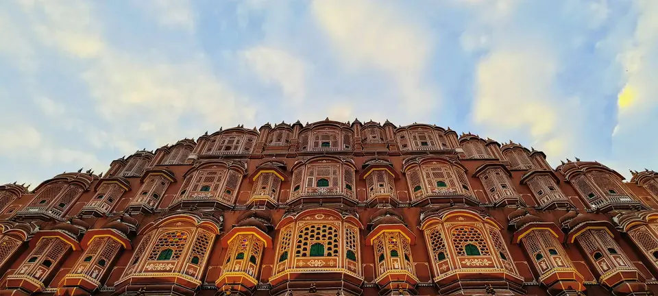 Pink sandstone facade of Hawa Mahal in Jaipur seen from below against a blue sky