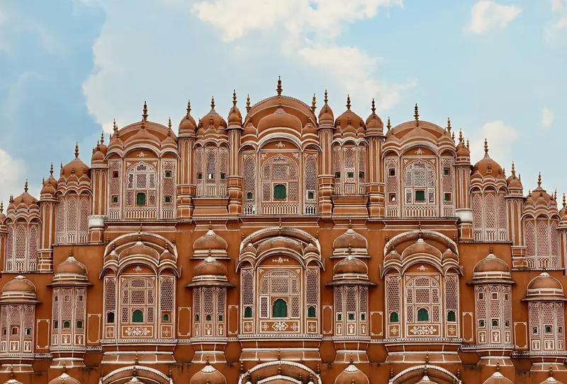 The pink sandstone facade of Hawa Mahal in Jaipur against blue sky and clouds