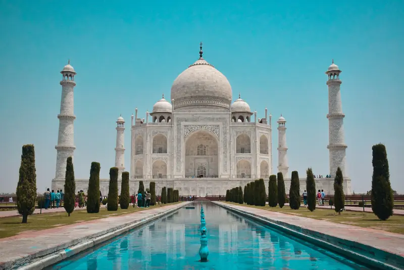 The Taj Mahal and its minarets above the reflecting pool under a blue sky